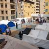 Children playing basketball and other games in a courtyard surrounded by white and blue tents at a temporary collective shelter in Beirut, Lebanon.