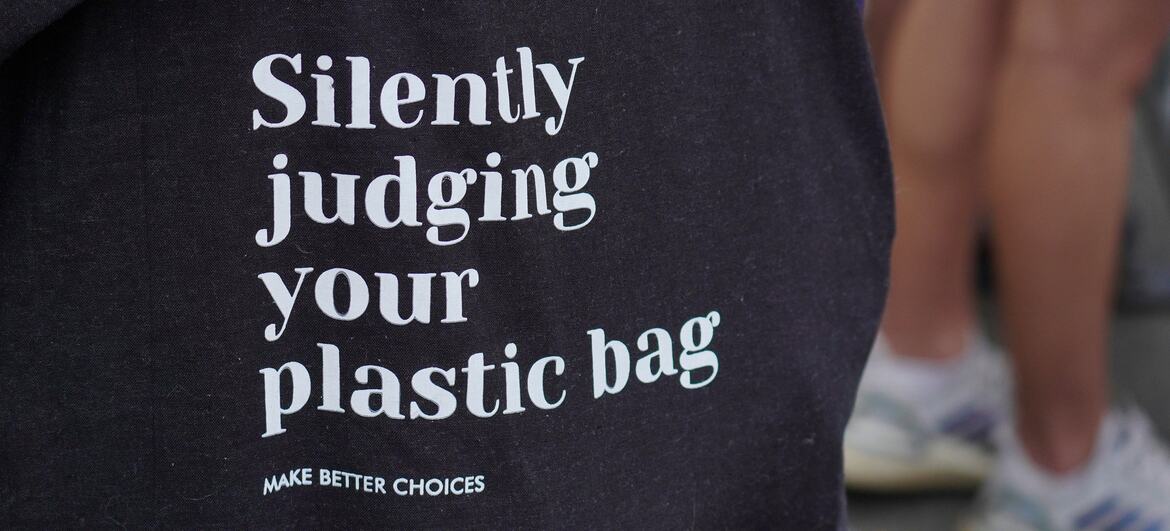 Close-up of a black tote bag with white text reading 'Silently judging your plastic bag' and 'MAKE BETTER CHOICES'.