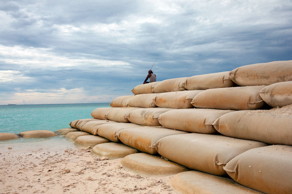 Pescador sentado em sacos de areia que protegem Tuvalu, nação insular do Oceano Pacífico, contra a erosão marinha