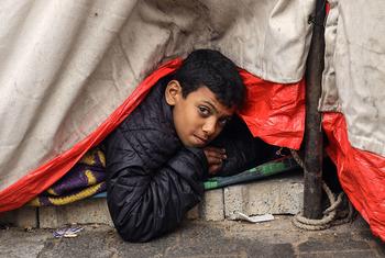 汗尤尼斯难民营，一名小男孩从他家的帐篷里往外看。
