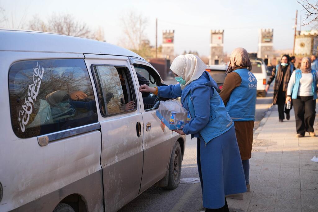 Des travailleurs humanitaires en uniforme bleu distribuent de l'eau en bouteille à des familles déplacées dans une camionnette près d'Alep, en Syrie.