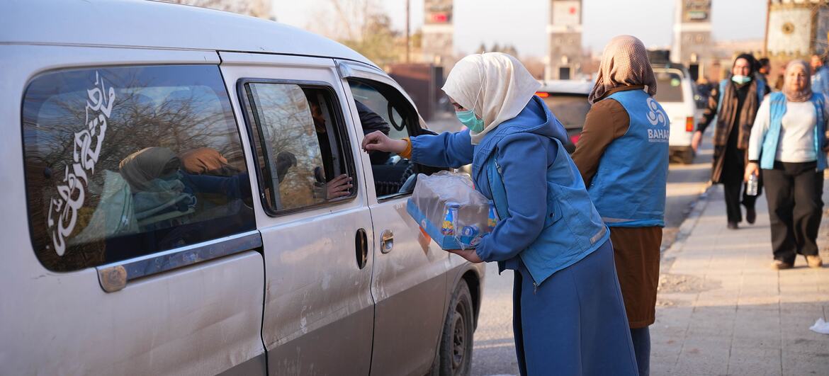 Aid workers in blue uniforms distribute bottled water to displaced families in a van near Aleppo City, Syria.