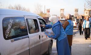 Aid workers in blue uniforms distribute bottled water to displaced families in a van near Aleppo City, Syria.