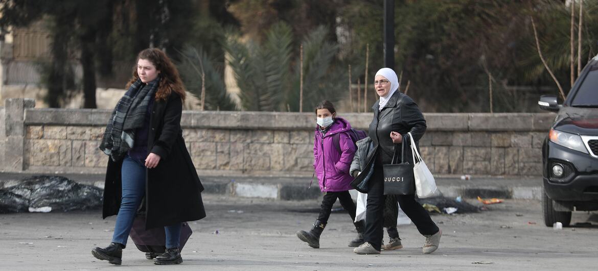 تسير النساء والأطفال عبر شارع مدمر في حلب، سوريا، وهم يحملون أغراضهم أثناء هربهم من النزاع والنزوح.