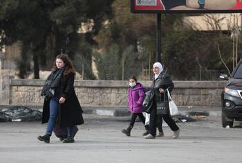 تسير النساء والأطفال عبر شارع مدمر في حلب، سوريا، وهم يحملون أغراضهم أثناء هربهم من النزاع والنزوح.