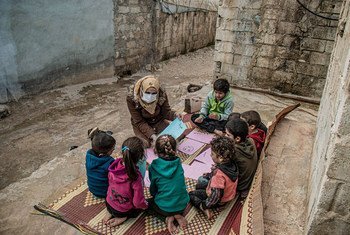 叙利亚西北部的流离失所者营地内，一位医务人员正与几名儿童交谈。