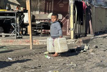 طفل صغير يحمل صفائح مياه في قطاع غزة.