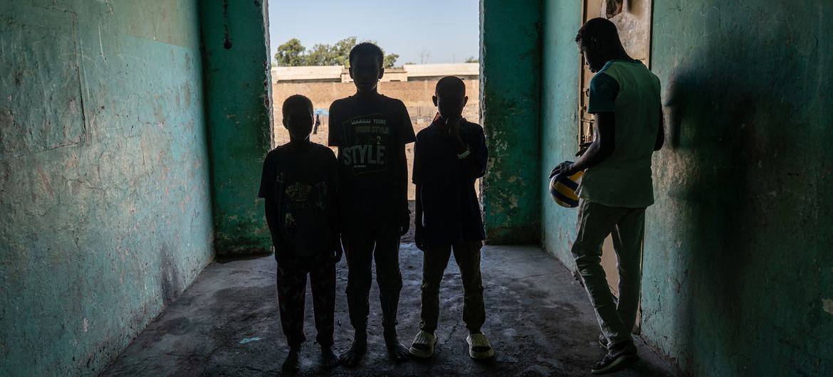 Quatre garçons se tiennent dans un couloir faiblement éclairé de l'orphelinat du centre Maygoma à New Haifa, au Soudan, l'un d'eux tenant un ballon.