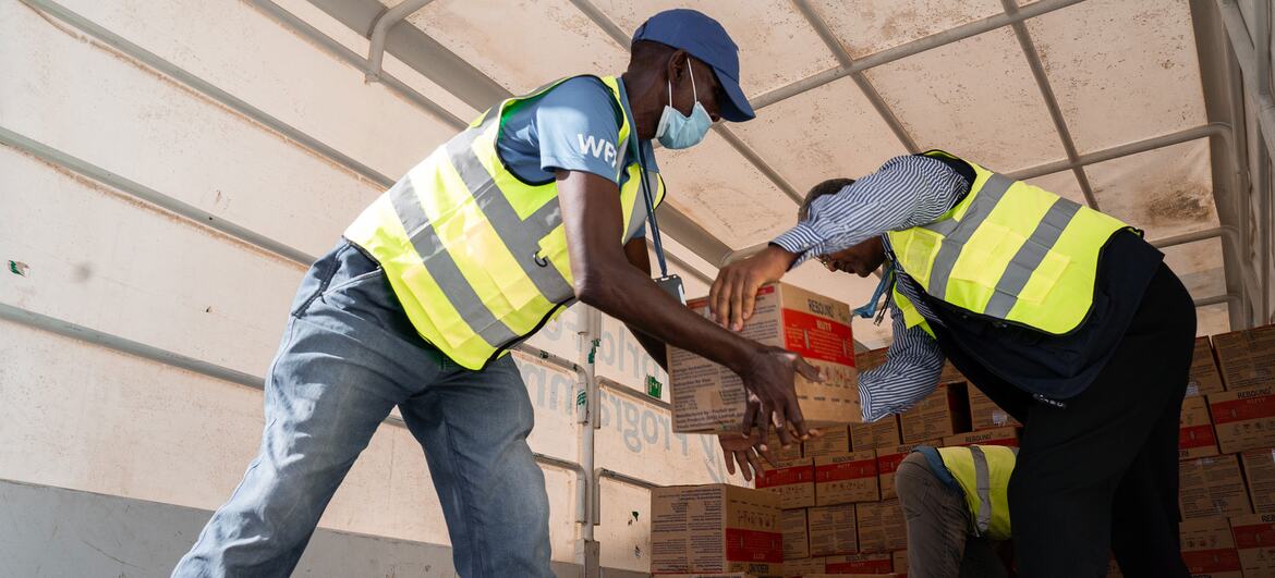 Le sergent Matthew Hollingworth, portant un gilet et un masque du PAM, reçoit une boîte de produits nutritionnels d'un autre travailleur humanitaire à l'intérieur d'un avion cargo en Somalie.