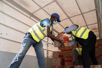 Le sergent Matthew Hollingworth, portant un gilet et un masque du PAM, reçoit une boîte de produits nutritionnels d'un autre travailleur humanitaire à l'intérieur d'un avion cargo en Somalie.