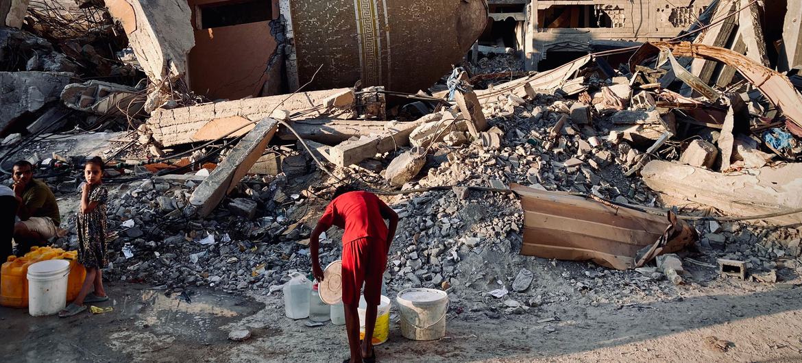 A person collects water in the midst of the ruins of Gaza.