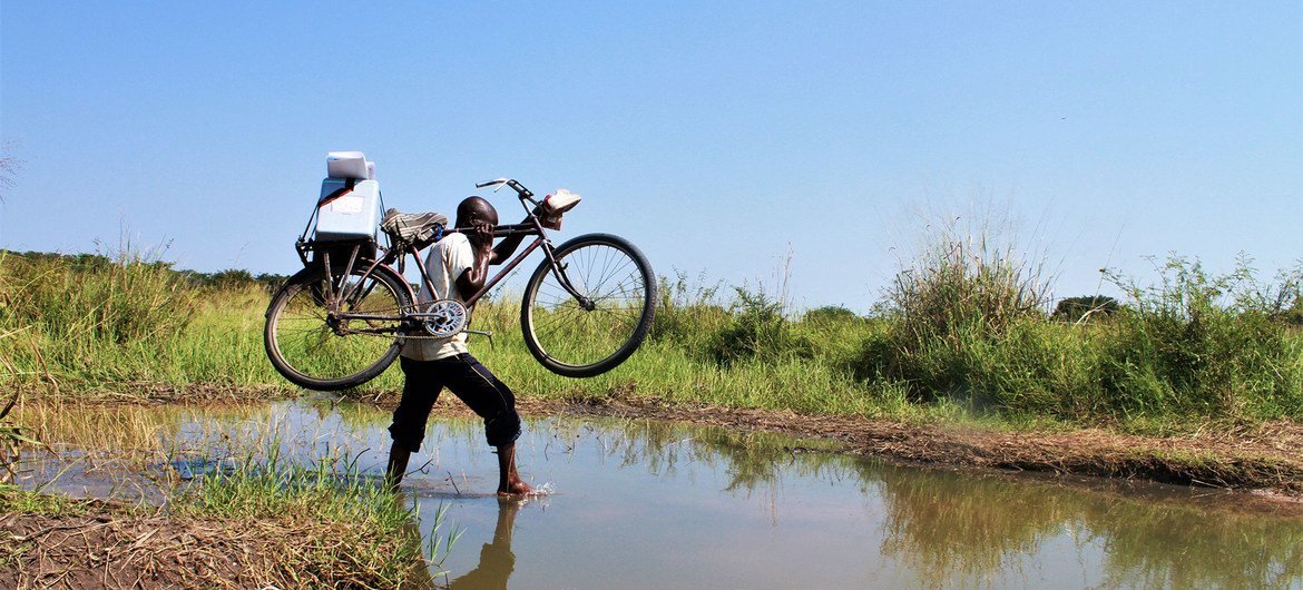 A health worker crosses a stream with his bike on his way to vaccinate children in Tanganyika Province in the Democratic Republic of the Congo.
