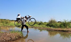 A health worker crosses a stream with his bike on his way to vaccinate children in Tanganyika Province in the Democratic Republic of the Congo.
