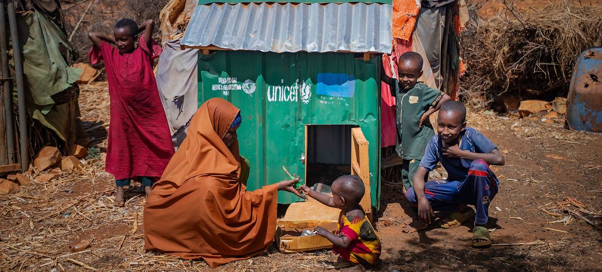 A Somali woman and children pose next to a green UNICEF chicken coop in a dry IDP settlement in Barwaaqo Camp, Baidoa, Somalia.