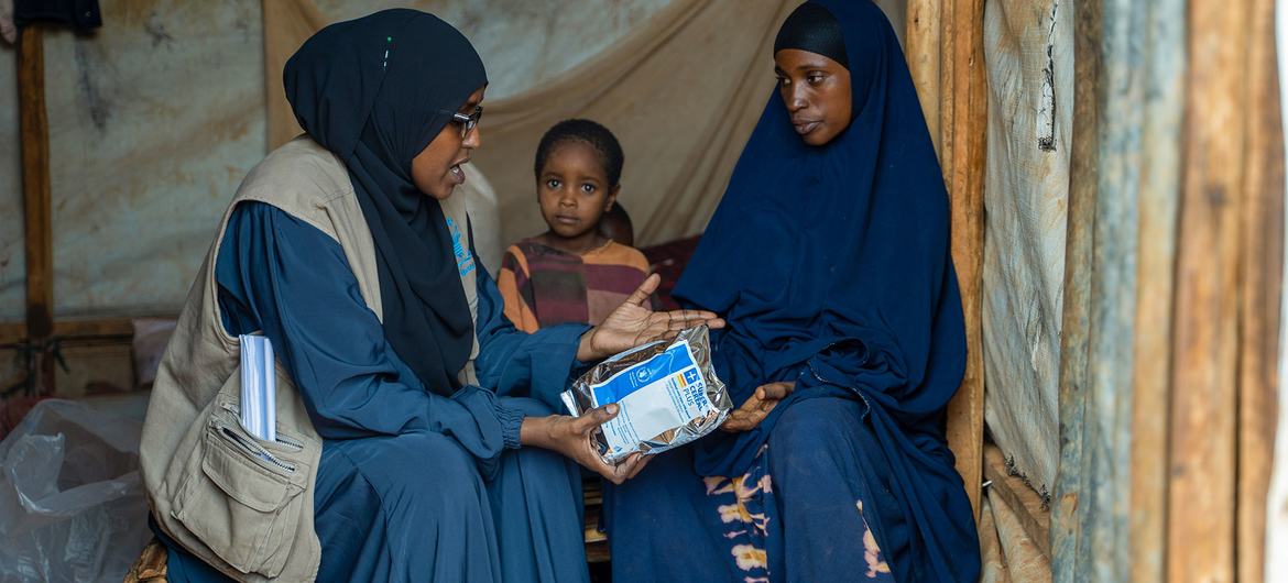 WFP staff member Ridwan Hassan distributes a food parcel to a mother and child in a temporary shelter at the Ladan IDP camp in Dollow, Somalia.