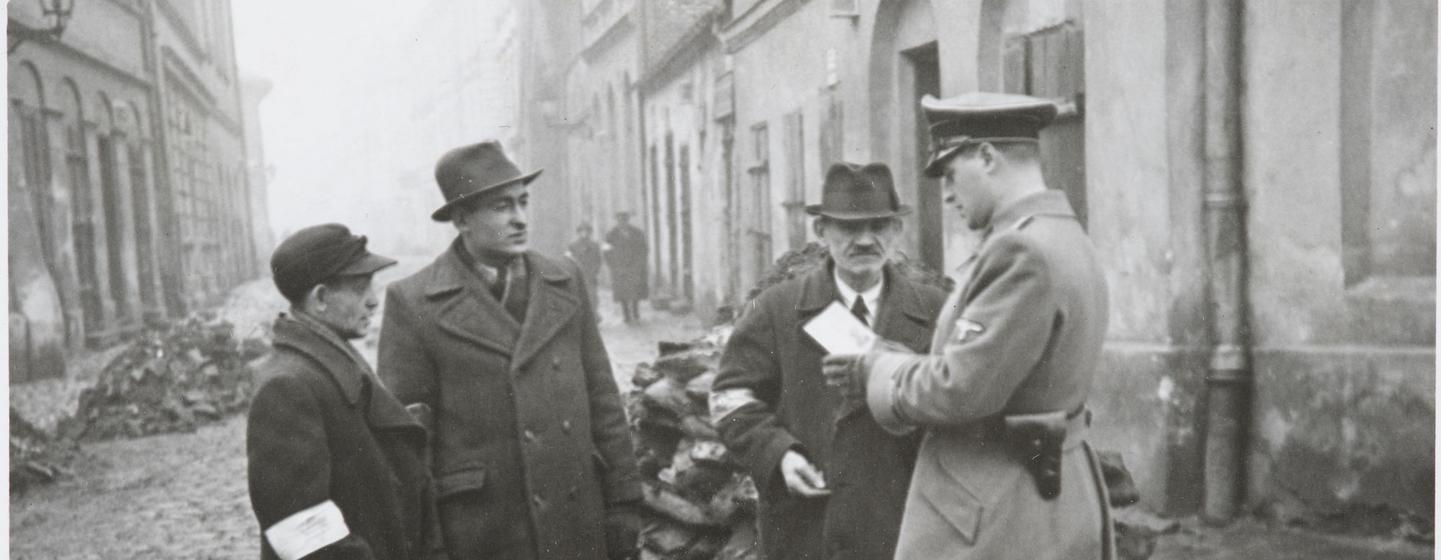A German policeman checks the identification papers of Jewish people in the Krakow ghetto. Poland. Circa 1941.