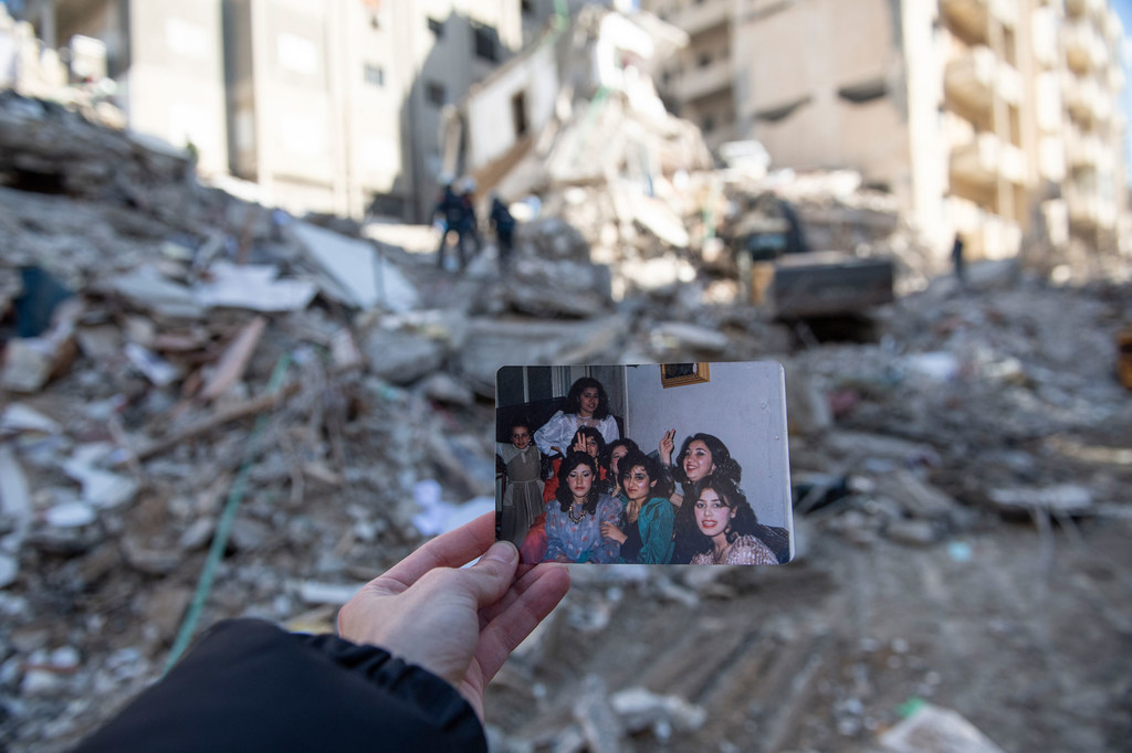 在叙利亚西北部，当地居民在曾经居住的建筑废墟前手举合影照。