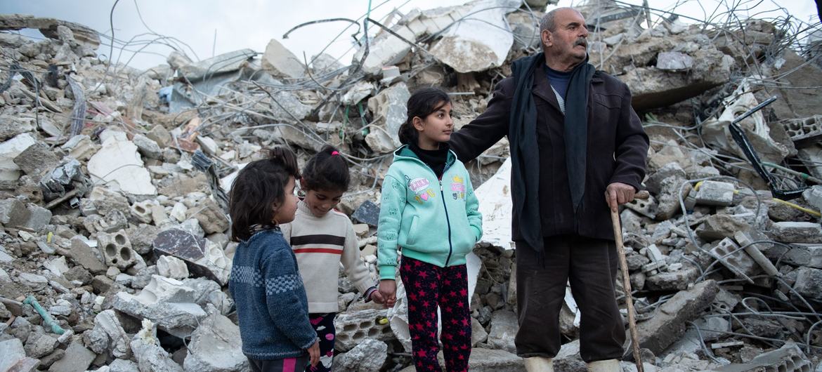 Uma família da área de Rumaila, no distrito de Jableh, no noroeste da Síria, próxima a sua casa destruída
