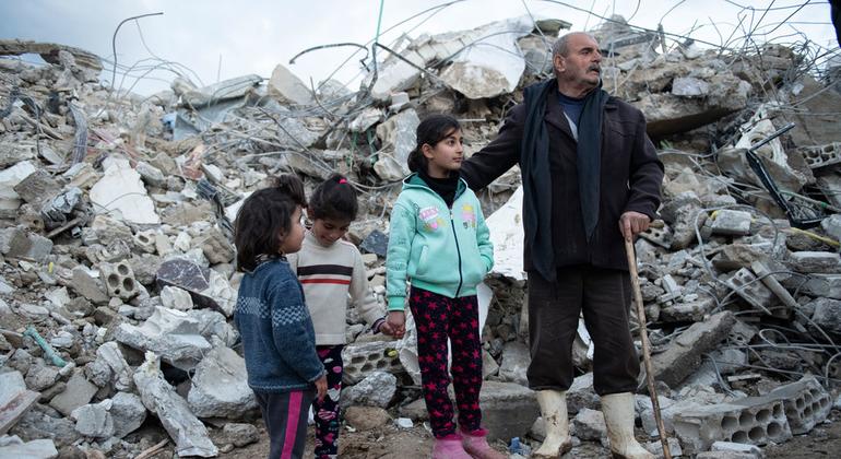 عائلة من منطقة الرميلة في قضاء جبلة شمال غرب سوريا تقف بالقرب من منزلها المدمر.