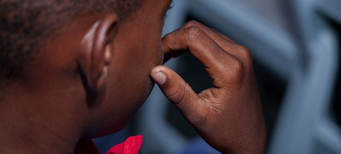 A close-up of a young boy in Haiti, his hand near his face, reflecting on the challenges of gang violence and the launch of the PREJEUNES programme to protect children from recruitment.