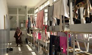 Una mujer con hiyab camina a través de un aula de una escuela en Beirut que se ha convertido en un refugio para familias desplazadas, cuyas ropas cuelgan de las literas donde viven las familias.