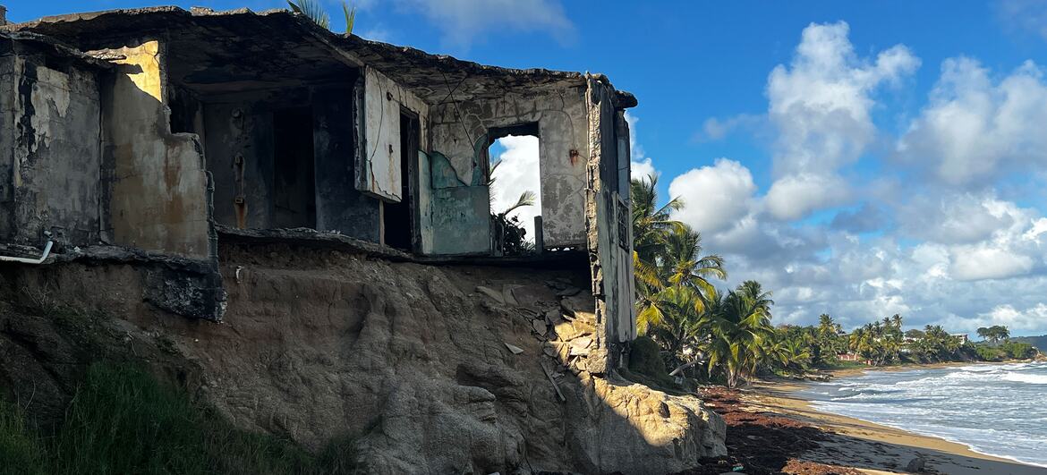 A destroyed building on a beach after a tsunami, showing severe coastal erosion and debris scattered on the sand.