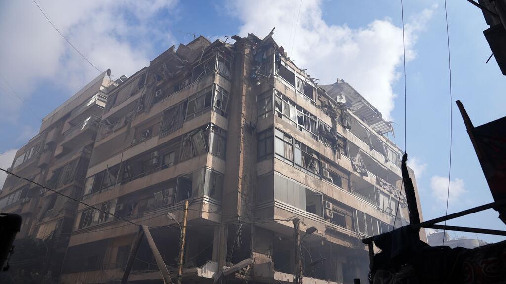 Un immeuble d'appartements de plusieurs étages à Beyrouth, au Liban, sévèrement endommagé par des frappes aériennes, montrant des étages effondrés, des fenêtres brisées et de la fumée contre un ciel bleu.