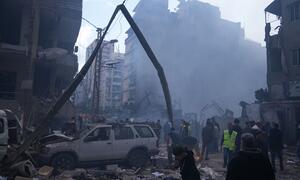 A scene of devastation in Beirut following airstrikes, showing collapsed buildings, smoke rising from rubble, and emergency personnel assessing the damage.