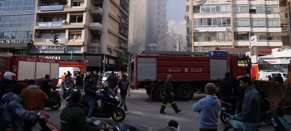 Vehículos de respuesta de emergencia y civiles se reúnen en una calle de Beirut entre humo y edificios dañados tras los ataques aéreos.