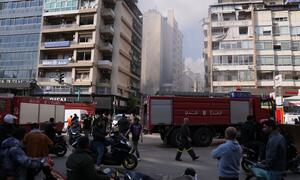 Vehículos de respuesta de emergencia y civiles se reúnen en una calle de Beirut entre humo y edificios dañados tras los ataques aéreos.