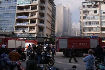 Vehículos de respuesta de emergencia y civiles se reúnen en una calle de Beirut entre humo y edificios dañados tras los ataques aéreos.