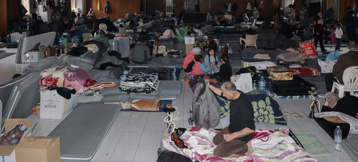 Displaced families living in an orphanage shelter in Lebanon, surrounded by mattresses and personal belongings after fleeing Israeli attacks.