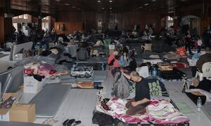 Displaced families living in an orphanage shelter in Lebanon, surrounded by mattresses and personal belongings after fleeing Israeli attacks.