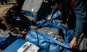 Wanaume wanaofungua mifuko mikubwa ya bluu yenye vitu vya misaada kama vitanda na blanketi wakati wa sherehe ya usambazaji wa UNHCR katika makao ya wakimbizi nchini Lebanon.