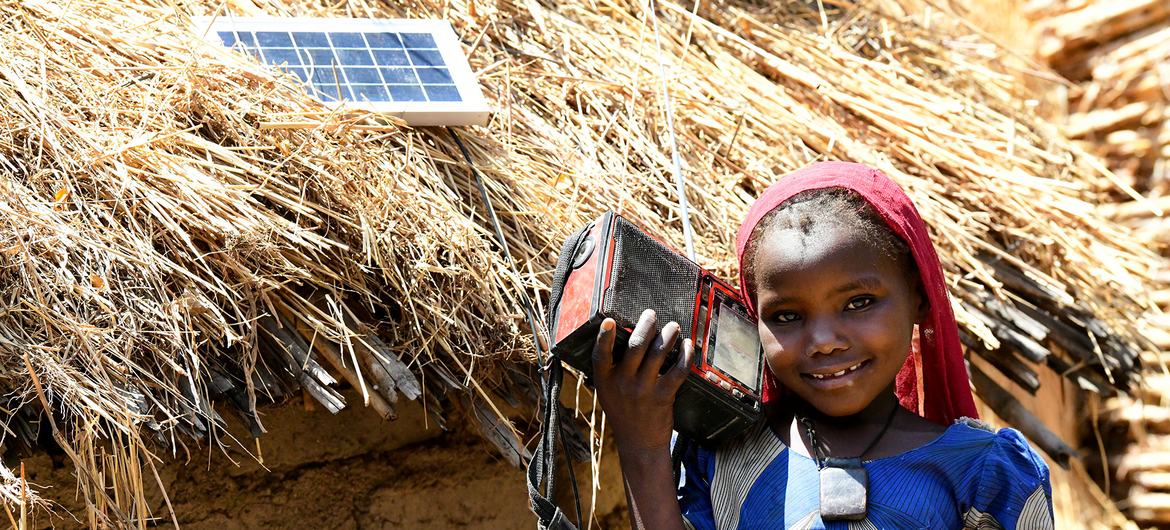 Dans la campagne tchadienne, une villagoise écoute un poste radio alimenté par un panneau photovoltaïque.