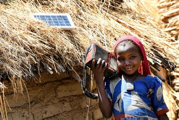 Dans la campagne tchadienne, une villagoise écoute un poste radio alimenté par un panneau photovoltaïque.solaire