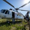 Uma mulher com máscara facial passa por um helicóptero branco do WFP (Programa Mundial de Alimentos) da UNHAS estacionado em um campo gramado no Haiti.