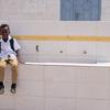 Um jovem refugiado somali, de uniforme escolar e mochila nas costas, está sentado em uma estrutura de azulejos em uma escola no Iêmen.