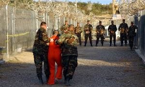 US Army Military Police escort a detainee to his cell in Camp X-Ray at Naval Base Guantanamo Bay, Cuba in 2002.