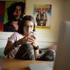 A teenage girl with glasses uses her smartphone while sitting in her room during an online class.