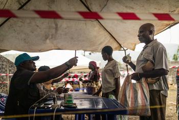 Un employé du PAM enregistre un bénéficiaire dans un point de distribution alimentaire à Sake, Goma, en RDC, tandis qu'un homme tient un colis alimentaire et qu'une autre personne fait la queue.