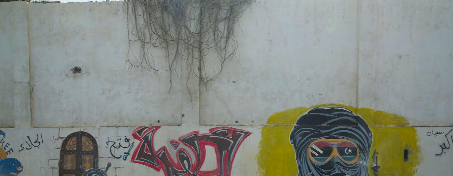 Une fresque murale sur un mur en béton à Tripoli représente un personnage masqué portant des lunettes de soleil et arborant le drapeau libyen.