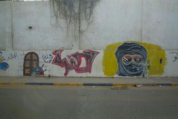 A mural on a concrete wall in Tripoli shows a masked figure wearing sunglasses with the Libyan flag.