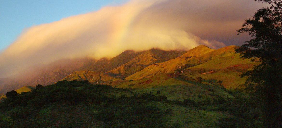 Uma vista das florestas tropicais de Atsinanana, em Madagascar, mostrando colinas verdejantes sob uma faixa de nuvens ao nascer do sol.