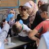 Uma criança recebe a vacina contra a poliomielite em uma clínica da UNRWA na Faixa de Gaza, cercada por mulheres e outras crianças.