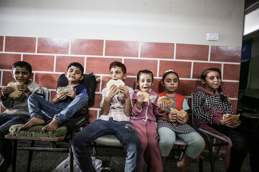 Des enfants de familles réfugiées dans une école de l'UNRWA à Gaza mangent du pain distribué par le Programme alimentaire mondial (PAM).
