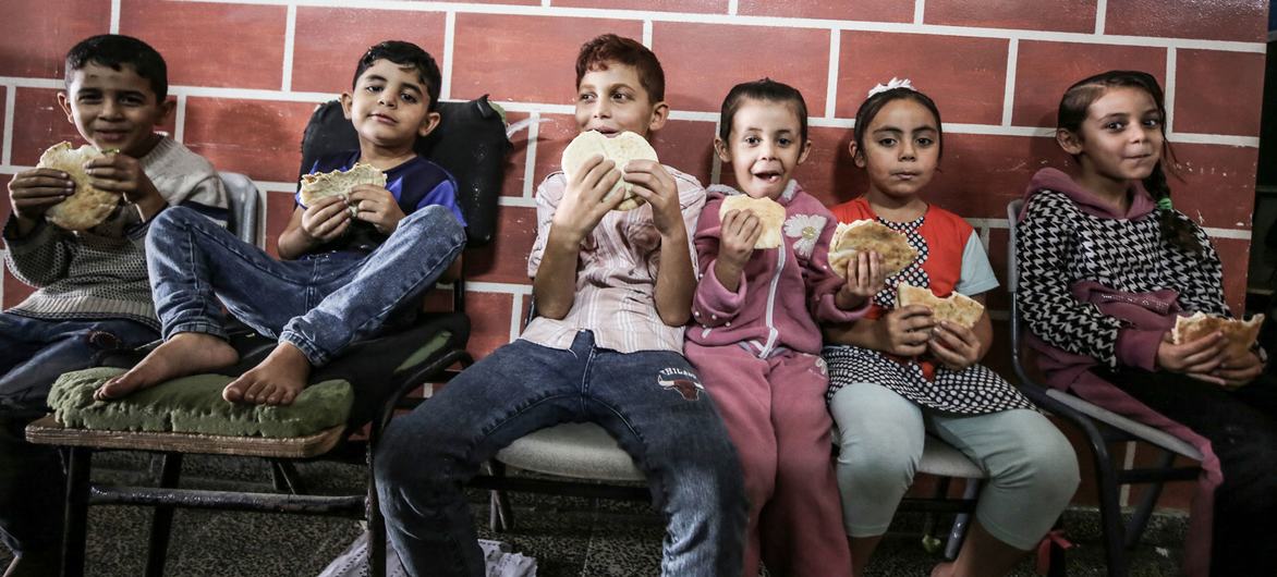 Crianças de famílias abrigadas numa escola da Unrwa em Gaza comem pão distribuído pelo Programa Mundial de Alimentos