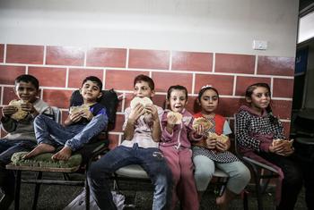 Children from families sheltering at an UNRWA school in Gaza eat bread distributed by the World Food Programme (WFP).