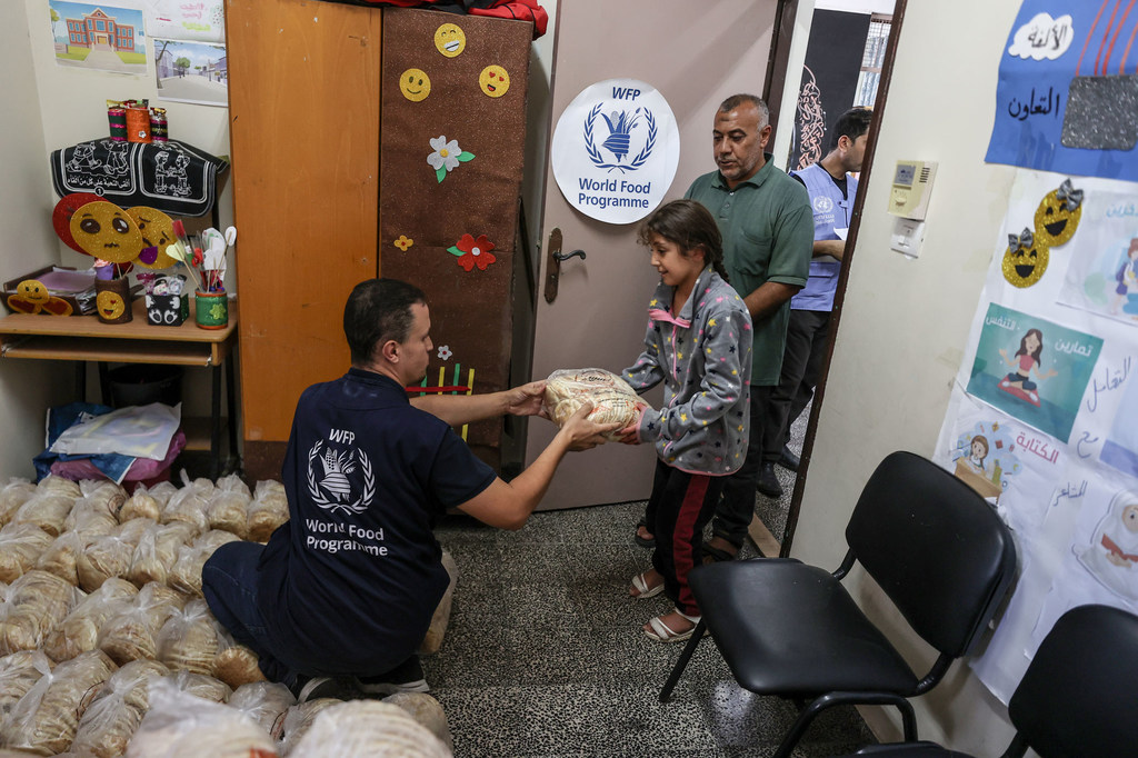 A World Food Programme (WFP) staff member distributes bread to a family sheltered at a UN school in Gaza.