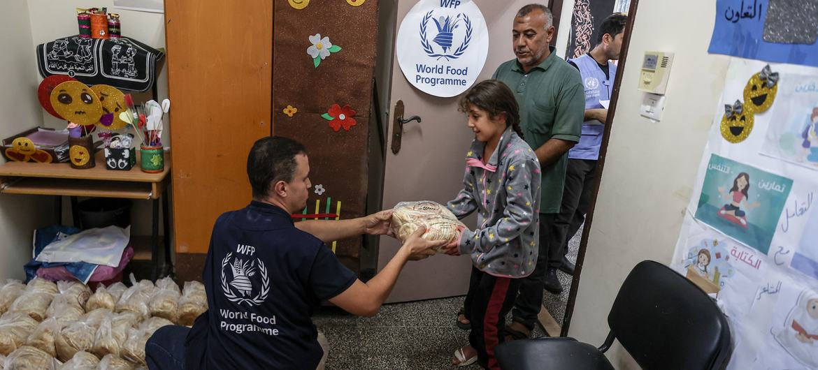 Um funcionário do Programa Mundial de Alimentos, PMA, distribui pão a uma família abrigada numa escola da ONU em Gaza